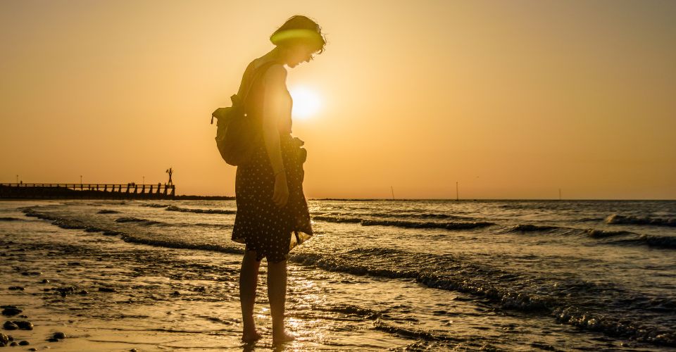 Petra kijkt uit over zee tijdens zonsondergang, een beeld dat vrijheid, ruimte en het volgen van je eigen pad symboliseert.
